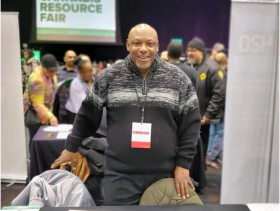 Smiling coalition member Douglas Kelly standing behind a table at a resource fair.