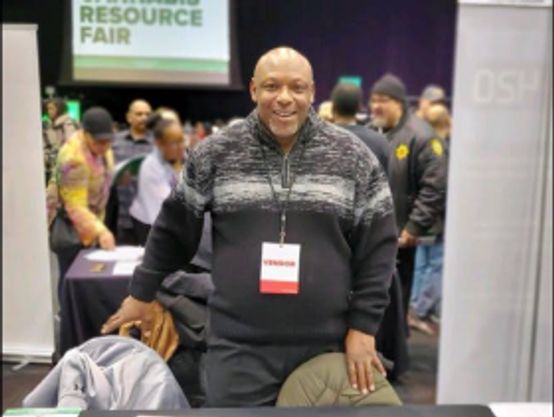 Smiling coalition member Douglas Kelly standing behind a table at a resource fair.